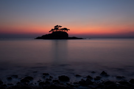 An island silhouette with pine trees and a long exposure view of the sea sunsetの写真素材