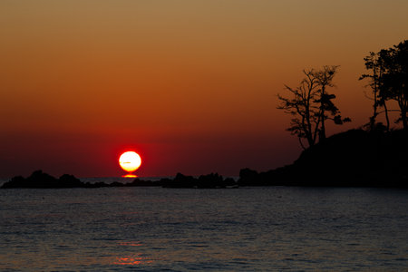 a round sun rising behind the island silhouetteの写真素材