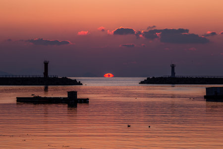 a sea sunrise with a lighthouse and a sun in the cloudsの写真素材