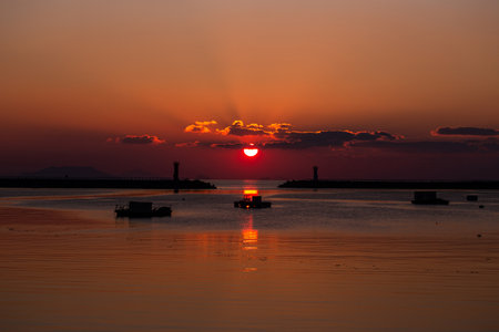 a sea sunrise with a lighthouse and a sun in the cloudsの写真素材