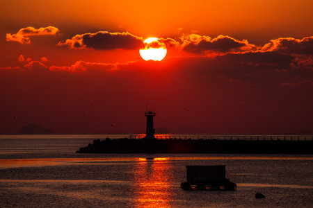 a sea sunrise with a lighthouse and a sun in the cloudsの写真素材