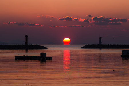 a sea sunrise with a lighthouse and a sun in the cloudsの写真素材