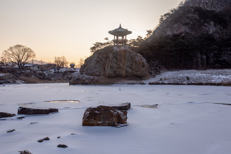 Winter scenery with frozen rivers, pavilions on rocks, and snow-covered mountainsの写真素材