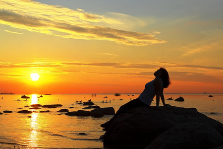 silhouette of the woman beach sea lake at sunset sitting on the stone looks at sun stretching the...