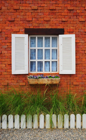 White window on brick wall with green grass and white fench