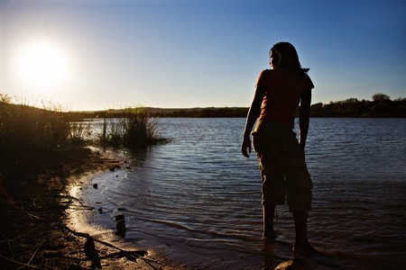 african girl washing her feet in the lake at sunsetの写真素材