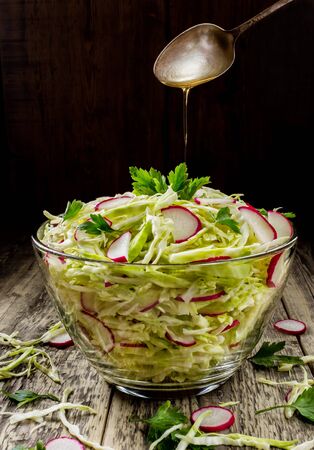 Fresh vegetable salad from chopped cabbage and radish roses. On a dark background of old boardsの写真素材