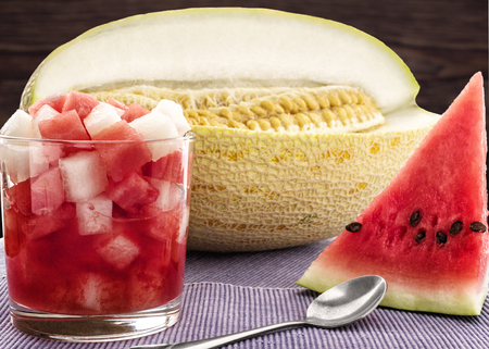 The cut pieces of melon and watermelon juice in a glass on blue napkinの写真素材