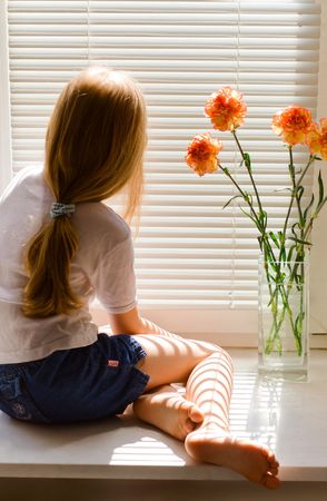 young blond girl sitting on a window-sillの写真素材