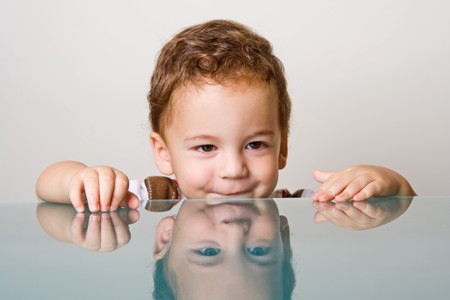 Small boy with curly hair behind glass tableの写真素材