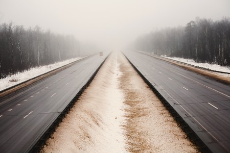 Snowy empty highway in the dark foggy forestの写真素材