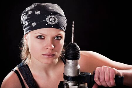 Severe young woman with a drill on black backgroundの写真素材