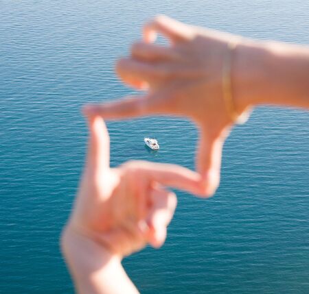 White ship in blue sea framed in fingersの写真素材