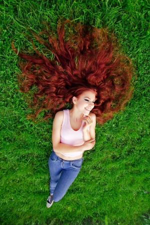 Girl with red hair lying on green grassの写真素材