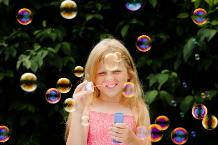 Small pretty girl is blowing soap bubbles