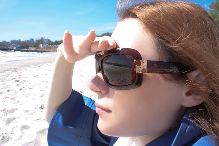 Girl in sunglasses sitting on a beach and look into the roar of the seaの写真素材