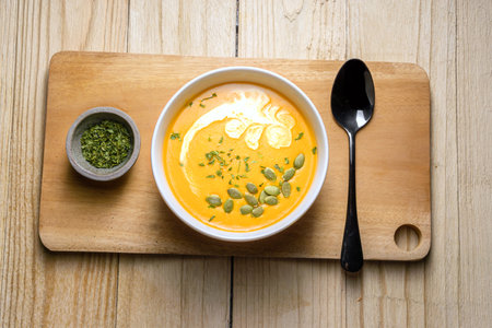 Yellow Pumpkin Soup with cream, pumpkin seed, and parsley on wooden background. Copy space. Top view.の写真素材