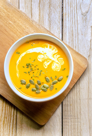 Yellow Pumpkin Soup with cream, pumpkin seed, parsley on wooden background. One bowl. Top view.の写真素材