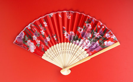 Red Oriental Chinese fan with a flower pattern closeup. Isolate on red background. Top view.の写真素材