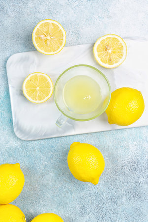 A cup of squeezed lemon juice and lemons, slices of lemons around. Bright background. Summer conceptの写真素材