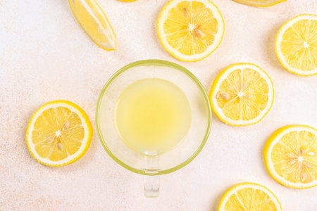 A cup of squeezed lemon juice and lemons, slices of lemons around. Bright background. Summer conceptの写真素材