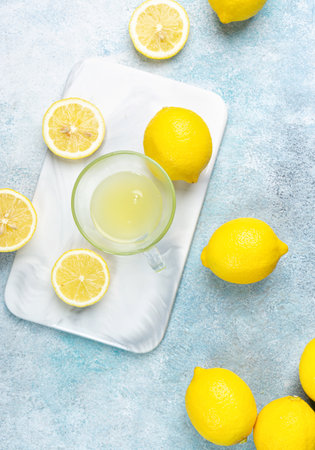 A cup of squeezed lemon juice and lemons, slices of lemons around. Bright background. Summer conceptの写真素材