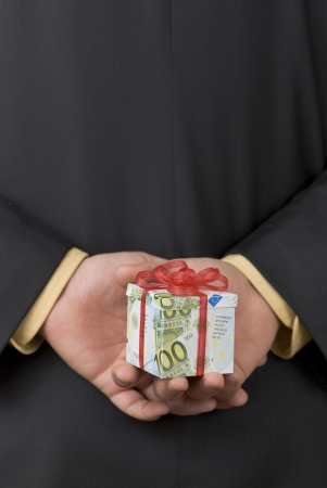 Man holding an expensive gift box wrapped in euro banknotes behind his backの写真素材