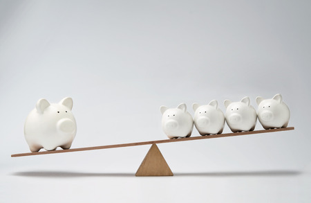 Small piggy banks and large piggy bank balancing on a seesawの写真素材