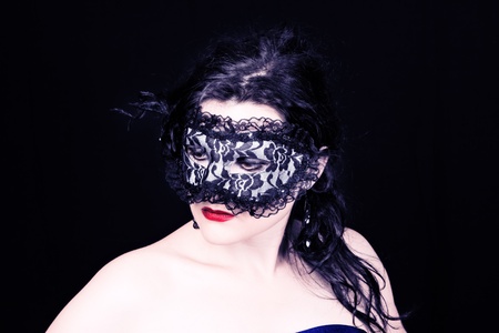 Mysterious brunette woman in mask with ruby lips on black backgroundの写真素材
