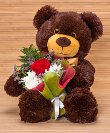 Smiling teddy bear holding beautiful floral bouquet in pawsの写真素材