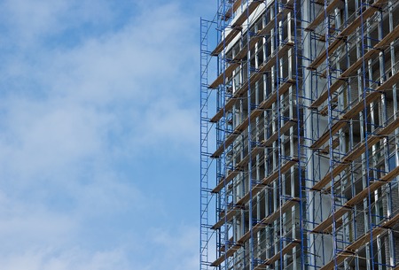 Facade of building under construction with scaffolding against blue sky