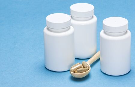 Nutritional supplements: capsules in a wooden spoon with white jars on a blue backgroundの写真素材