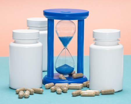 Anti-aging supplements concept: scattered capsules with white plastic jars and hourglass