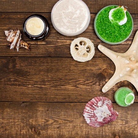 Spa cosmetics and accessories: sea salt, loofah, skin care cream, natural scrubs with shells and starfish on wooden planks. Top view. Corner frame, copy spaceの写真素材
