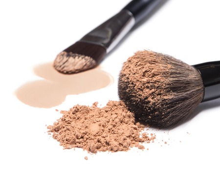 Close-up of makeup brushes with loose cosmetic powder and smeared liquid foundation on white background. Focus on the foregroundの写真素材