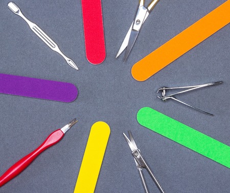 Various manicure tools laid out as circle on gray textured background. Nail clippers, nail and cuticle scissors, colored nail files, double ended cuticle trimmer / pusher, cuticle removerの写真素材