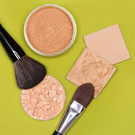 Set of makeup products to even out skin tone and complexion: concealer, correcting powder, jar of loose cosmetic powder, crushed compact powder with makeup brushes on herbal green textured surfaceの写真素材