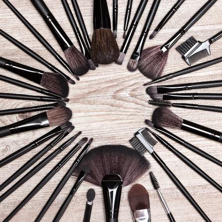 Various makeup brushes laid out as circle on shabby wooden surface. Professional tools of make-up artist. Round frame. Copy space in the center. Beauty backgroundの写真素材