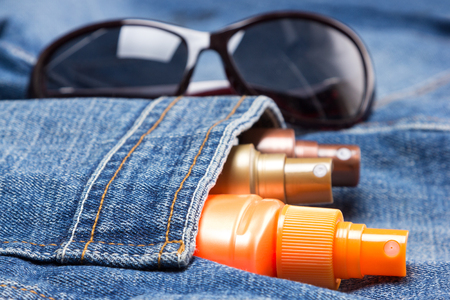 Cosmetic sunscreen products in jeans pocket on the background of sunglasses. Skin care cosmetics...