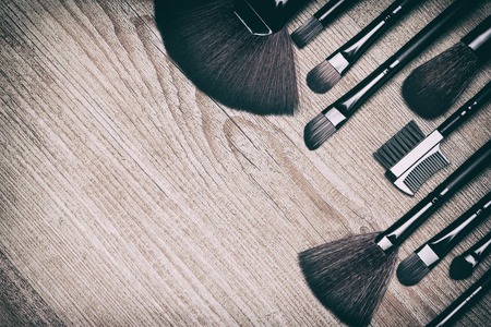 Set of various makeup brushes: for applying powder, eyeshadow, eyebrow brushes, fan brushes and others. Professional tools of makeup artist on shabby wooden surface. Copy space. Retro style processingの写真素材