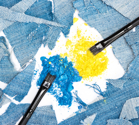 Close-up of makeup brushes with crushed compact blue and yellow eyeshadow surrounded by rags of...