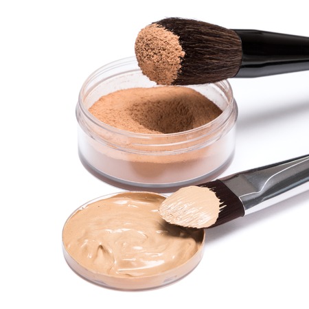 Liquid foundation and open jar of loose cosmetic powder with brushes on white background, side view. Makeup products to even out skin tone and complexionの写真素材