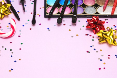 Christmas party makeup. Bright color glitter eyeshadow, mascara, eyeliner, lip gloss, lip liners, applicator, brushes with candy cane, gift wrap bows and confetti. Shallow depth of field. Copy spaceの写真素材