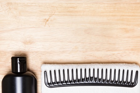 Hair care and styling background. Black bottle, wide tooth comb and white terry cloth towel on...