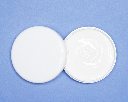 Close-up of jar with open lid filled with skin care cream on blue backgroundの写真素材