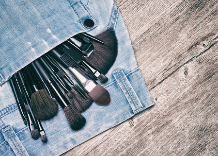 Professional tools of makeup artist in blue jeans pocket on shabby wooden surface. Make up brushes...