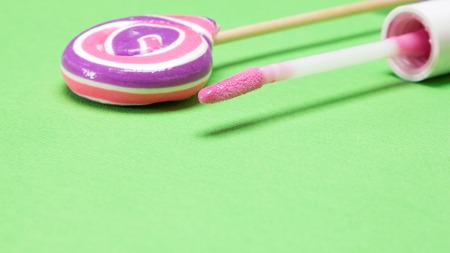 Close up of pink lip gloss with lollipop on green textured background. Shallow depth of field, copy spaceの写真素材