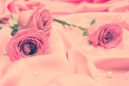 Close-up of rose flowers on pink satin fabric with bead strand. Vintage toning. Gentle romantic backgroundの写真素材