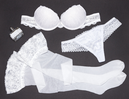 White lingerie set with perfume on gray background. Strapless underwire bra, lace thong pantie and stockings. Accessories of brideの写真素材