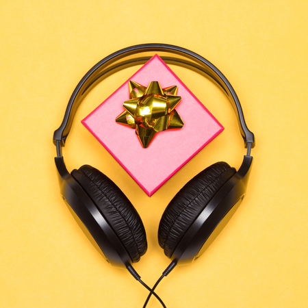 Headphones with gift box on bright yellow background. Music as present. Holiday songsの写真素材